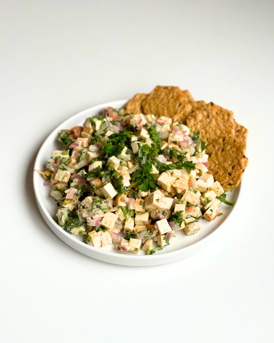 Tofu salad on a white plate with crackers on the side