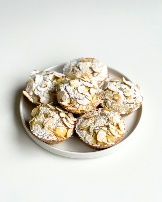 six almond croissant muffins on a white plate with a white background