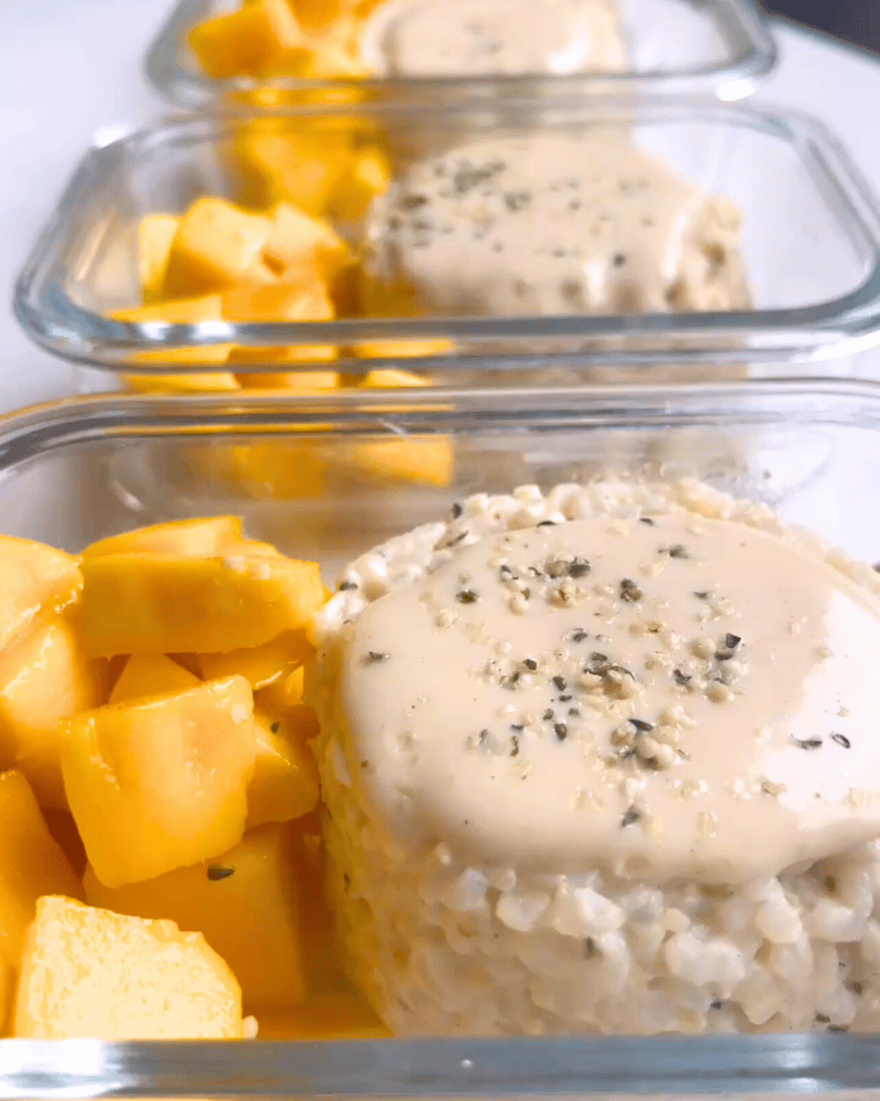 Glass containers with coconut sticky rice and mango chunks on a white surface