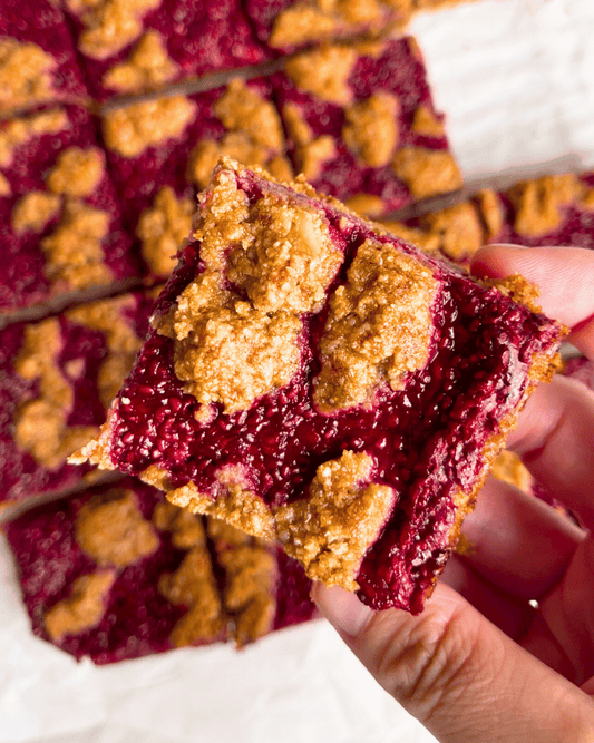 An up close picture of a hand holding a raspberry jam oat bar cover a plate of oat bars
