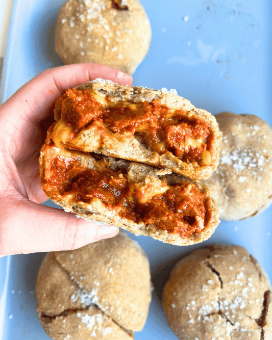 vegan pepperoni pizza bun sliced in half and being held by a hand above the baking tray