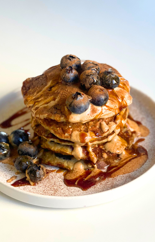 Stack of pancake topped with blueberries, maple syrup and peanut butter on a white plate with a white background