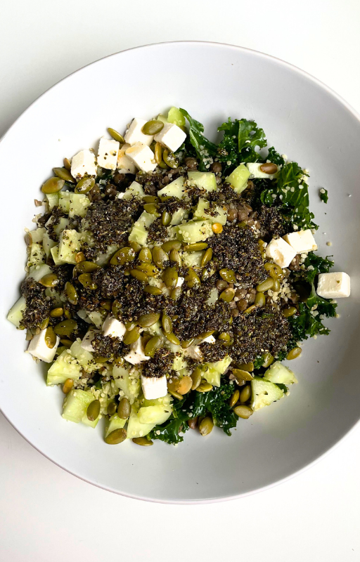 Kale salad with black quinoa topped with vegan feta cheese in a white plate on a white background