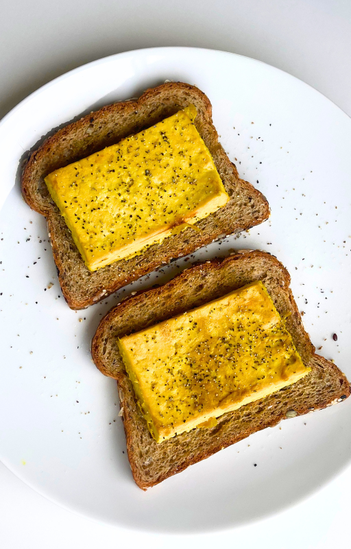 Two pieces of baked tofu patty and toast on a white plate