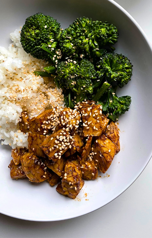 Tempeh, broccoli and white rice topped with sesame seeds on a white plate