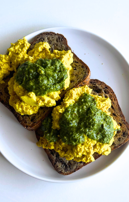 Two slices of gluten free toast with tofu scrambled on top on a white plate
