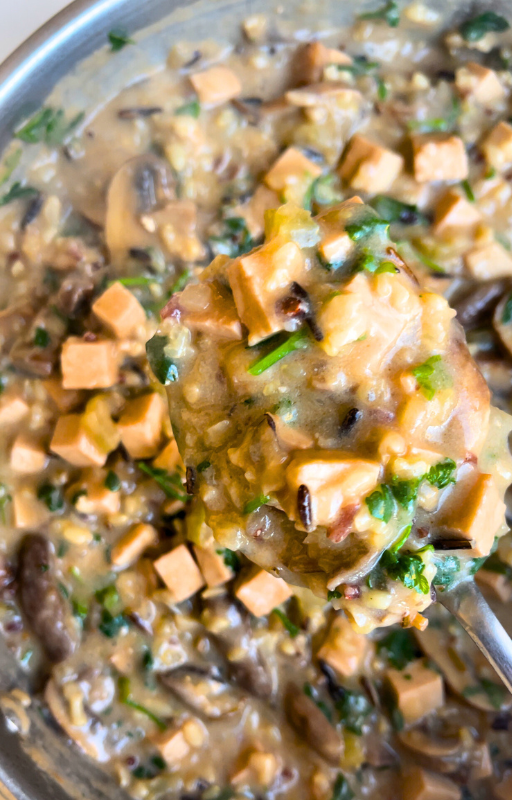 Holding a spoon full of vegan wild rice soup above a frying pan with wild rice soup in it