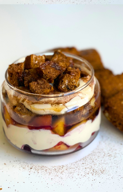 Vegan yogurt parfait with peach in a glass jar on a white table with some cookies on the background