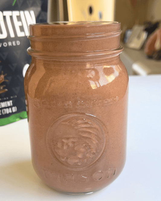 chocolate peanut butter smoothie in a glass jar with vedge protein powder in the background