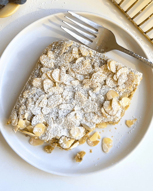 A slice of almond croissant baked oats on a white plate with a fork.