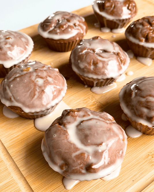 apple fritter muffins with icing sugar glaze, on a wood cutting board