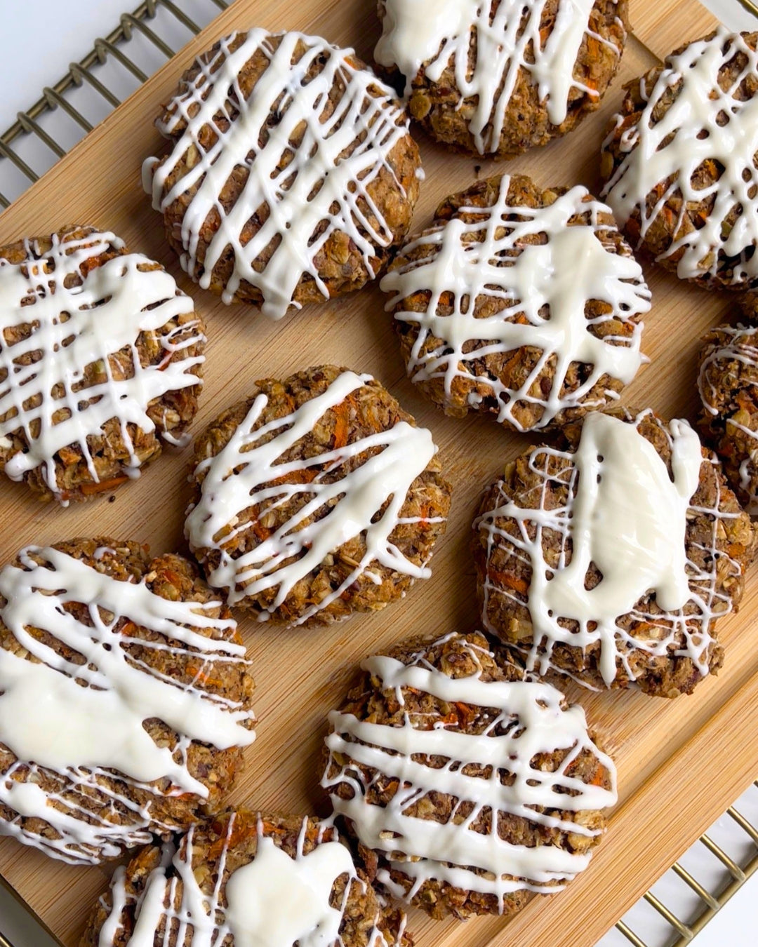 carrot cake protein cookies with a white chocolate drizzle on top sitting on a wire rack