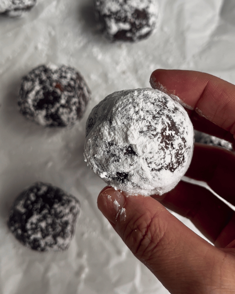 a hand holding a brownie bite protein ball over a bunch of other chocolate balls 