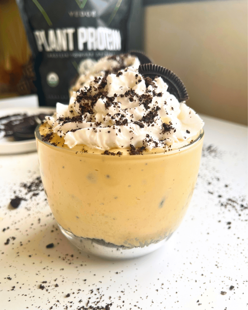Vegan cookies and cream protein pudding jars on a white counter with cookie crumbs all over the white counter underneath and a Vedge protein powder bag in the background