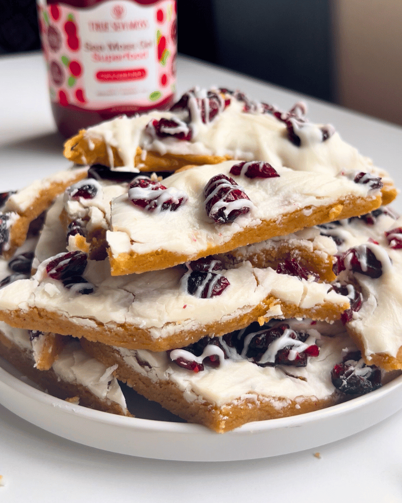 cranberry bliss bar sliced into chunks and piled on a white plate with a jar of cranberry true sea moss gel in the background 