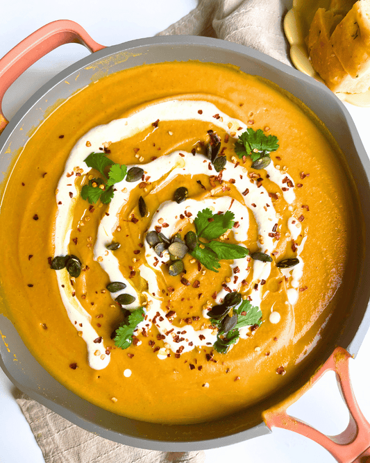 pumpkin soup in a pink pot with cilantro on top and cashew cream drizzle