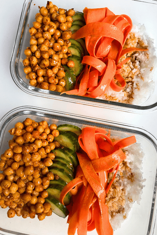 peanut chickpeas with rice, cucumber, carrots, and sauce in a glass meal prep container.