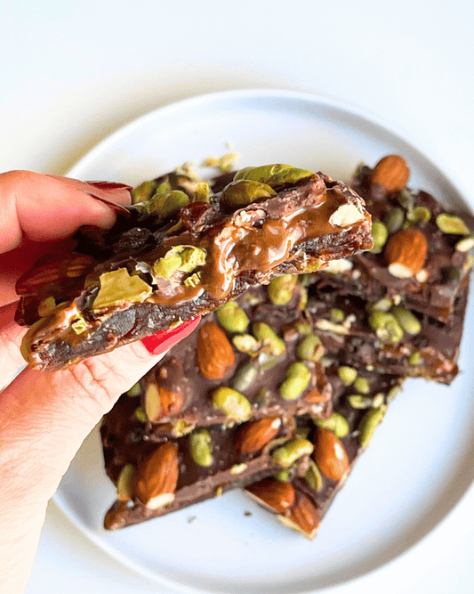 a hand holding slices of protein date bark up close over a plate of them