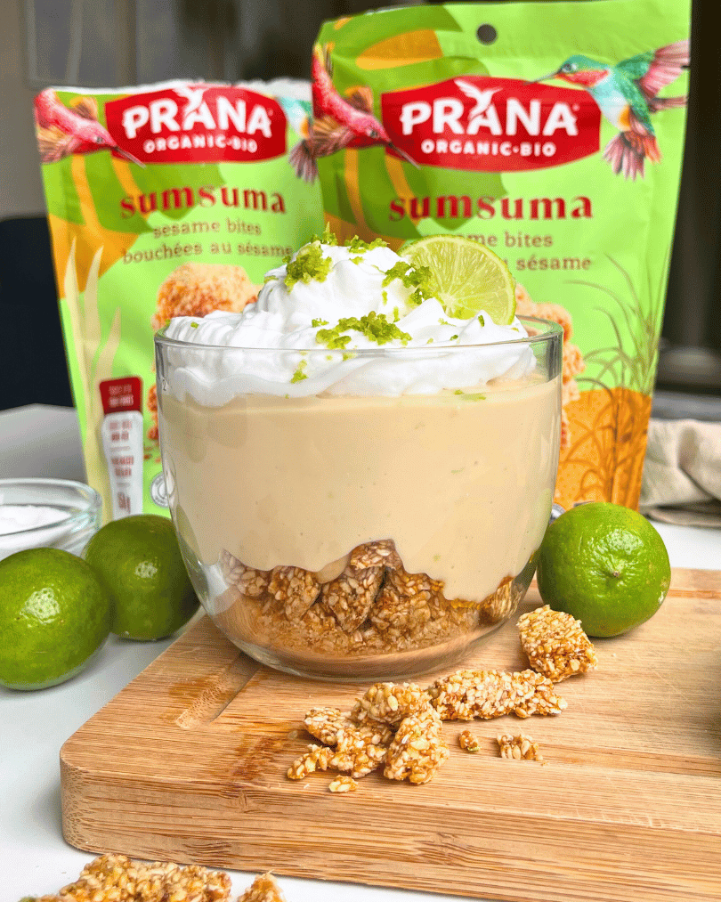 high protein yogurt bowl, key lime cheesecake flavour, in a glass jar on a wood cutting board with Prana Sumsuma Square packaging in the background.
