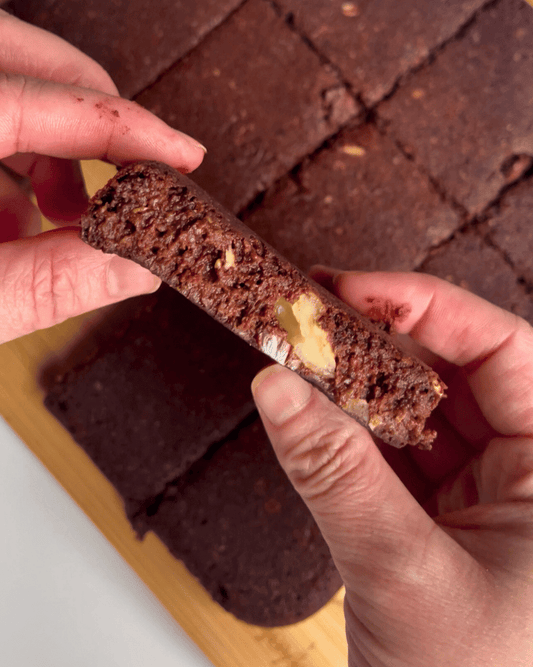 two hands holding a lactation brownie up close over the tray of sliced brownies