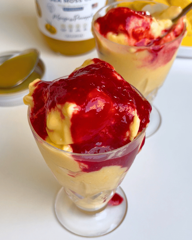 mango frozen yogurt in a glass cup with raspberry sauce on top.
