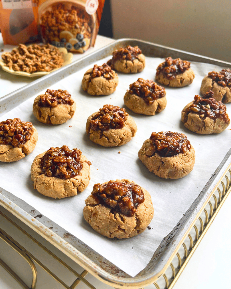 baked pecan pie protein cookies on a baking tray on a gold cooling rack with granola on a plate in the background