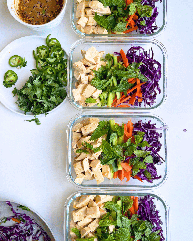 spring roll salad meal prep in 4 glass containers on a white surface.