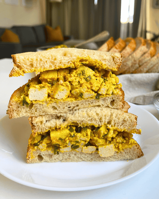 tofu egg salad sandwich sliced open and stacked on top of each other on a white plate.