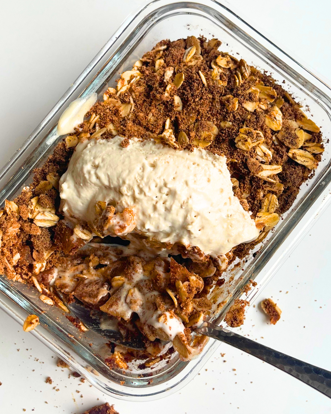 vegan apple crisp with coconut whip on top and spoon digging into it