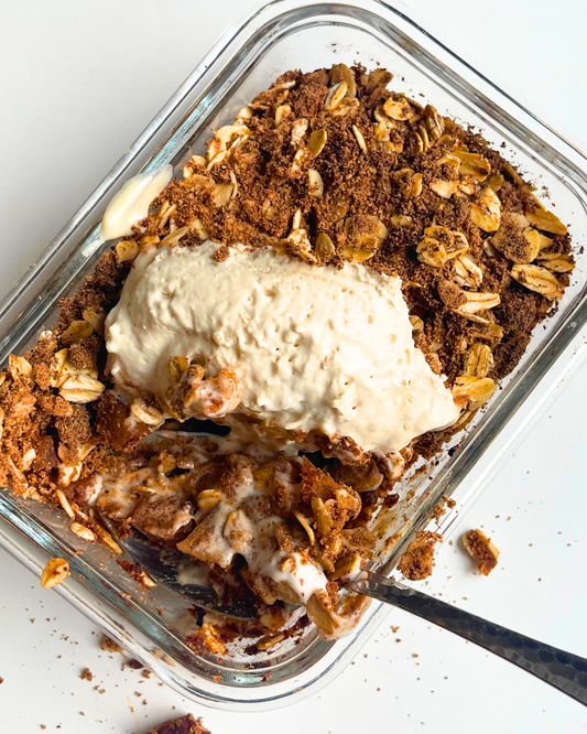 vegan apple crisp with coconut whip on top and spoon digging into it