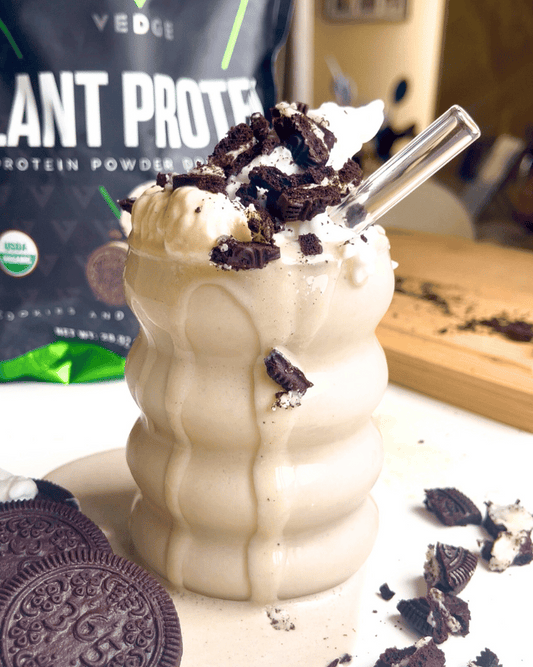 vegan cookies and cream protein shake in a glass with a straw and vedge nutrition protein bag in the background.