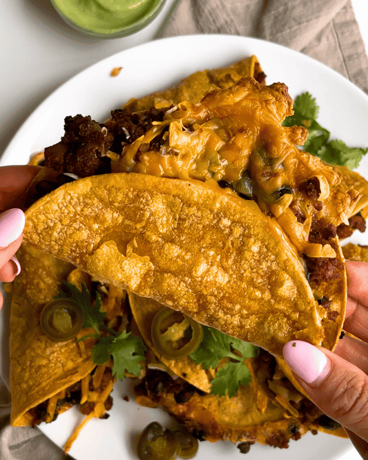 vegan crispy baked tacos held in a hand with pink nails over a plate of more tacos