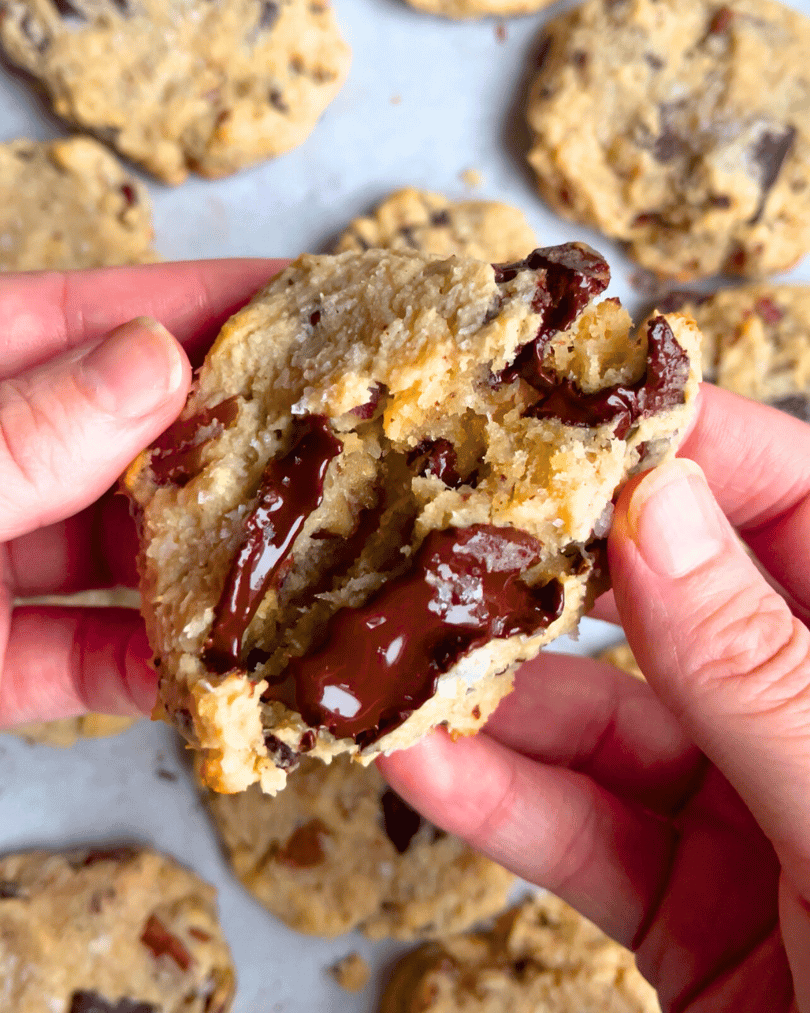 two hands breaking a part a chocolate chip filled vegan magic cookie