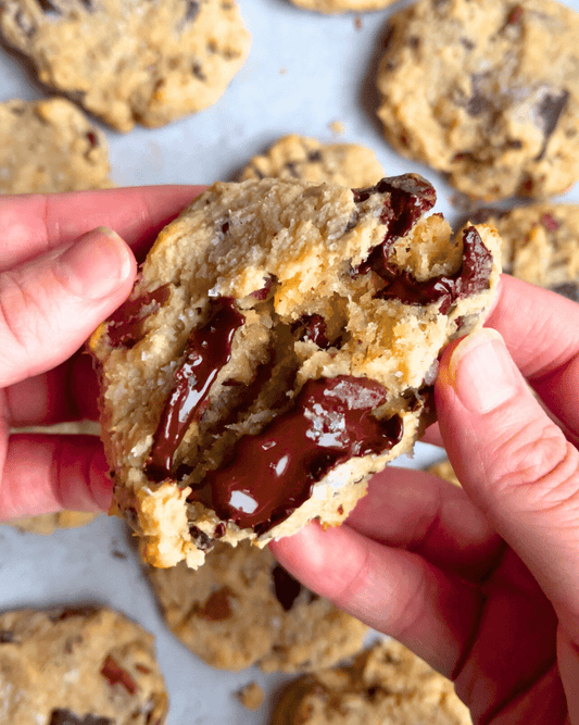 two hands breaking a part a chocolate chip filled vegan magic cookie