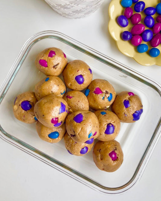 mini egg energy balls in a glass container next to a small yellow plate with chocolate candy covered peanuts on it