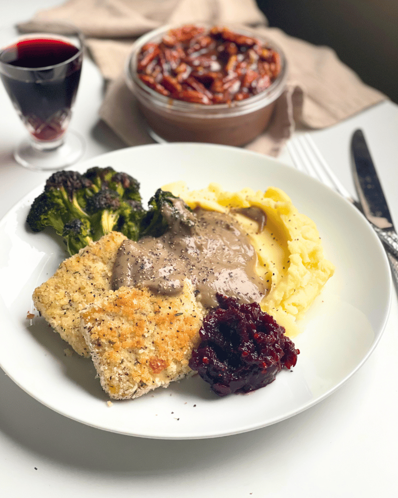 full vegan thanksgiving dinner on a white plate with cherry juice in a glass and chocolate pecan pudding in the background