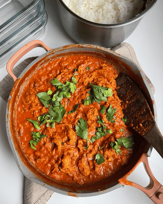 overhead shot of vegan tikka masala in a pink and grey lined pan with a wooden spatula inside ready to serve
