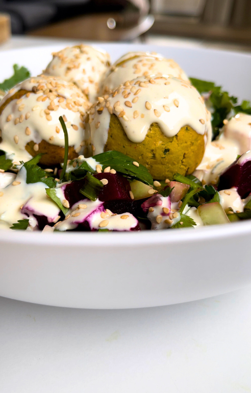 Four felafels on a salad topped with vegan white sauce and sesame seeds in a white plate 