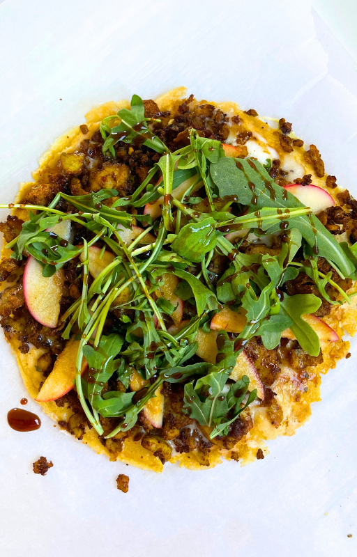 Vegan grain free pizza topped with arugula on a white background
