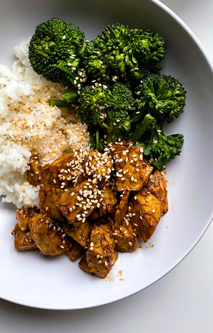 Tempeh, broccoli and white rice topped with sesame seeds on a white plate