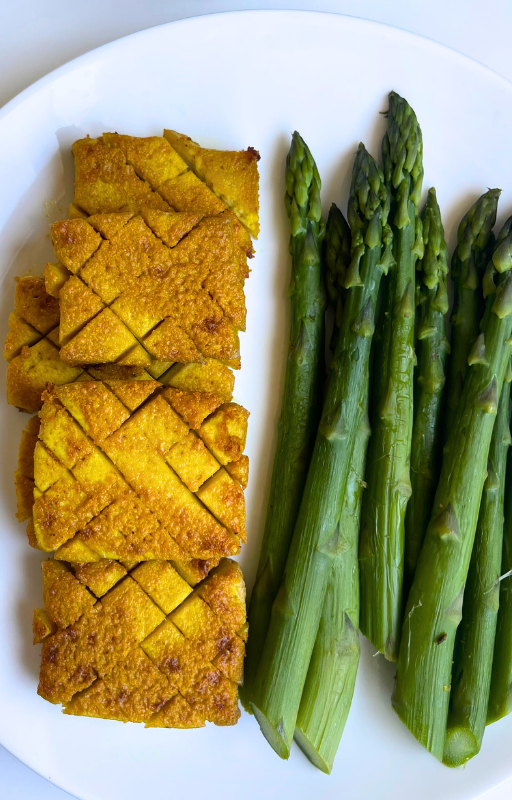Six pieces of baked tofu with asparagus on a white plate