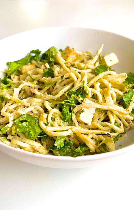 A bowl of noodles with herbs and tofu in a white plate on a white background