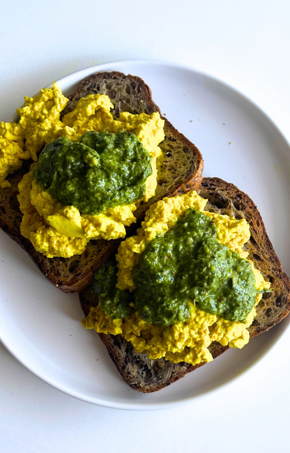 Two slices of gluten free toast with tofu scrambled on top on a white plate