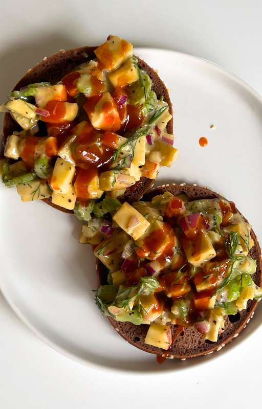 Two pieces of bagels with vegan tuna salad on top on a white plate